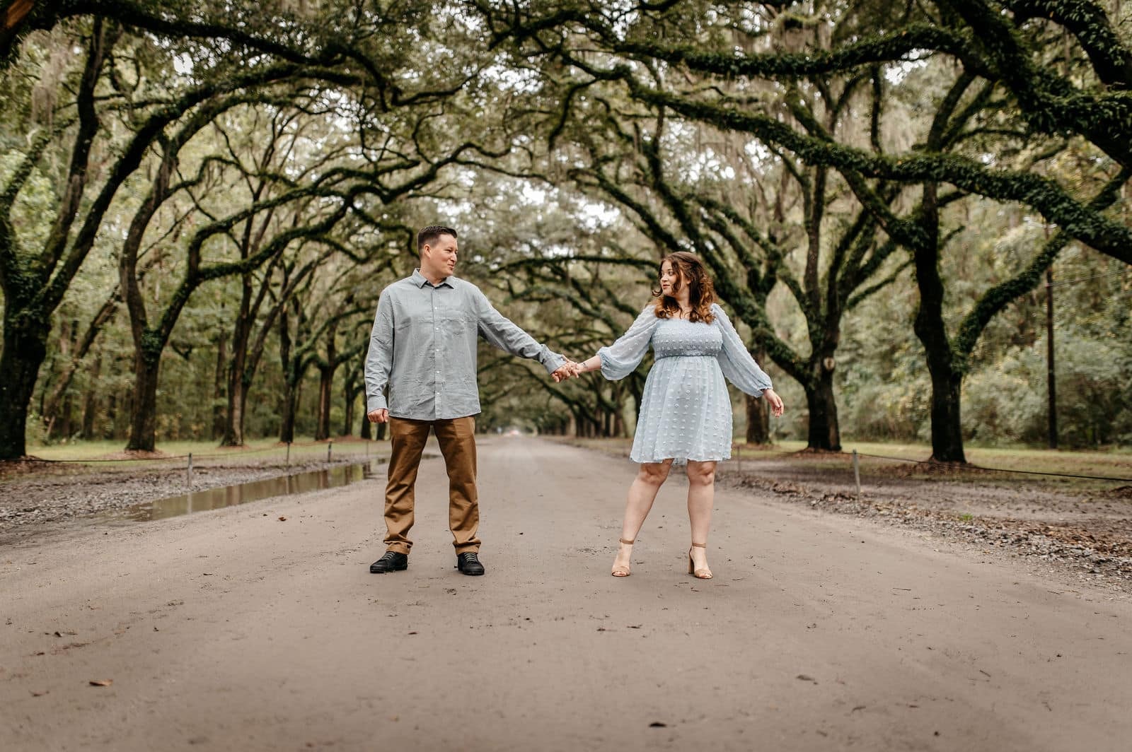 Engaged couple holding hands beneath large oak trees during an outdoor session captured by a Georgia wedding videographer.