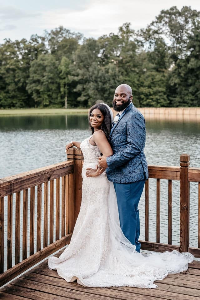 Bride and groom on a lakeside deck, her lace train spread out behind her.