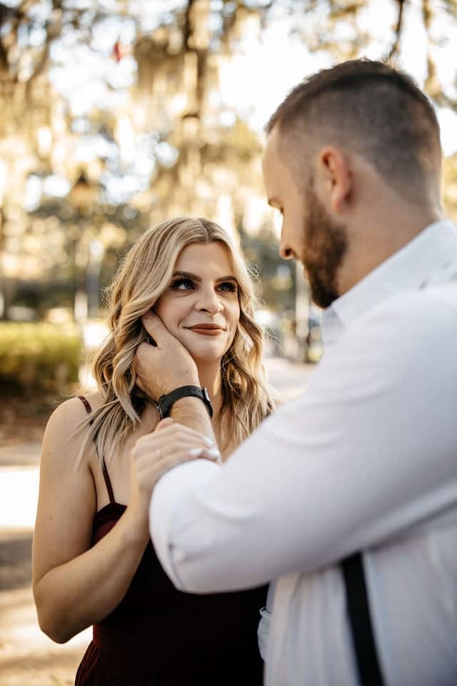 A man cupping his fiancee's face during an engagement session under Spanish moss.