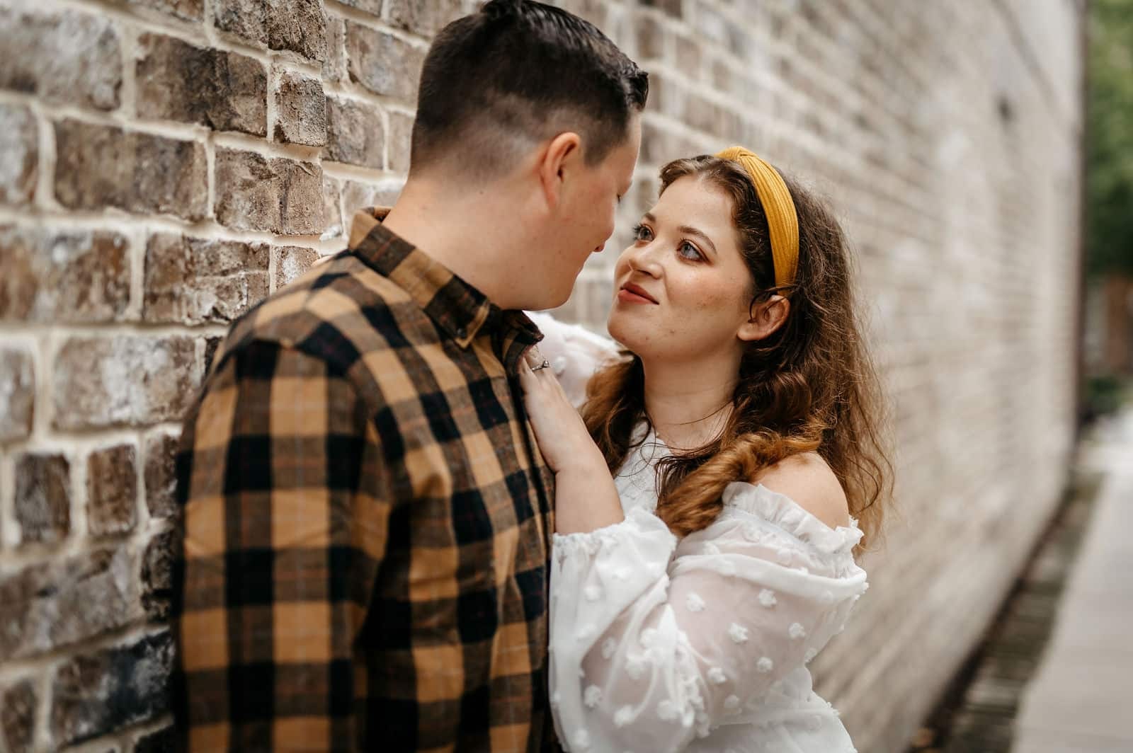 Engaged couple sharing a romantic moment beside a brick wall during a Georgia engagement photography session.