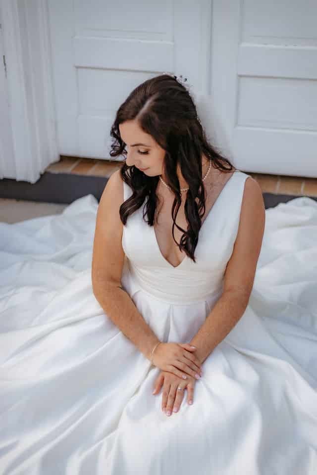 A bride seated on the floor with her satin skirt spread around her.