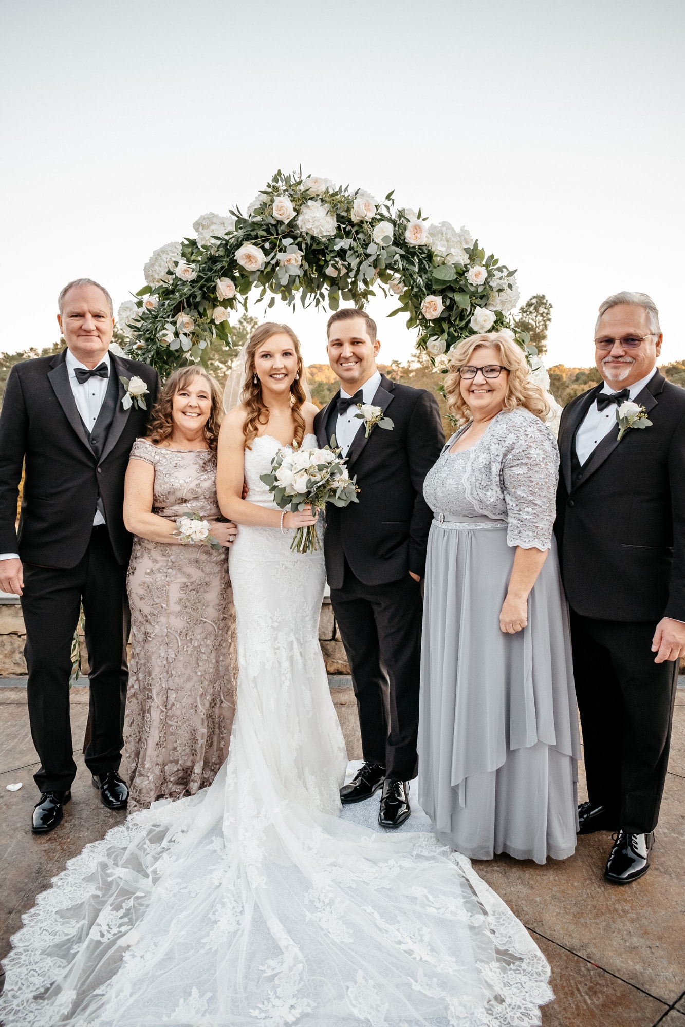 A bride photographed with her family in a row in front of a white and green floral arch.