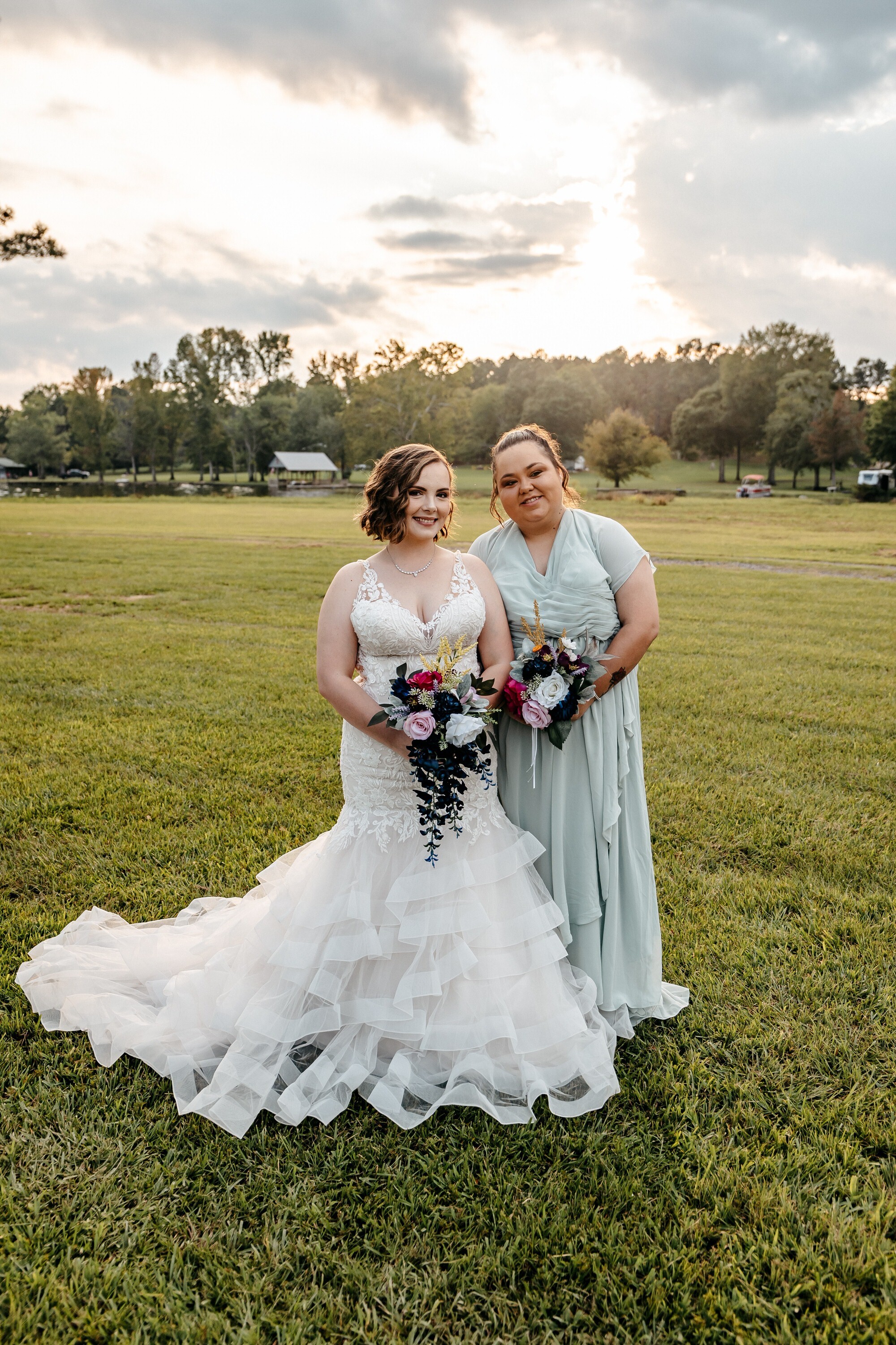 A bride in a white mermaid gown holds a colorful bouqet whilet posing with one of her bridesmaids a one of the best outdoor wedding venues in georgia