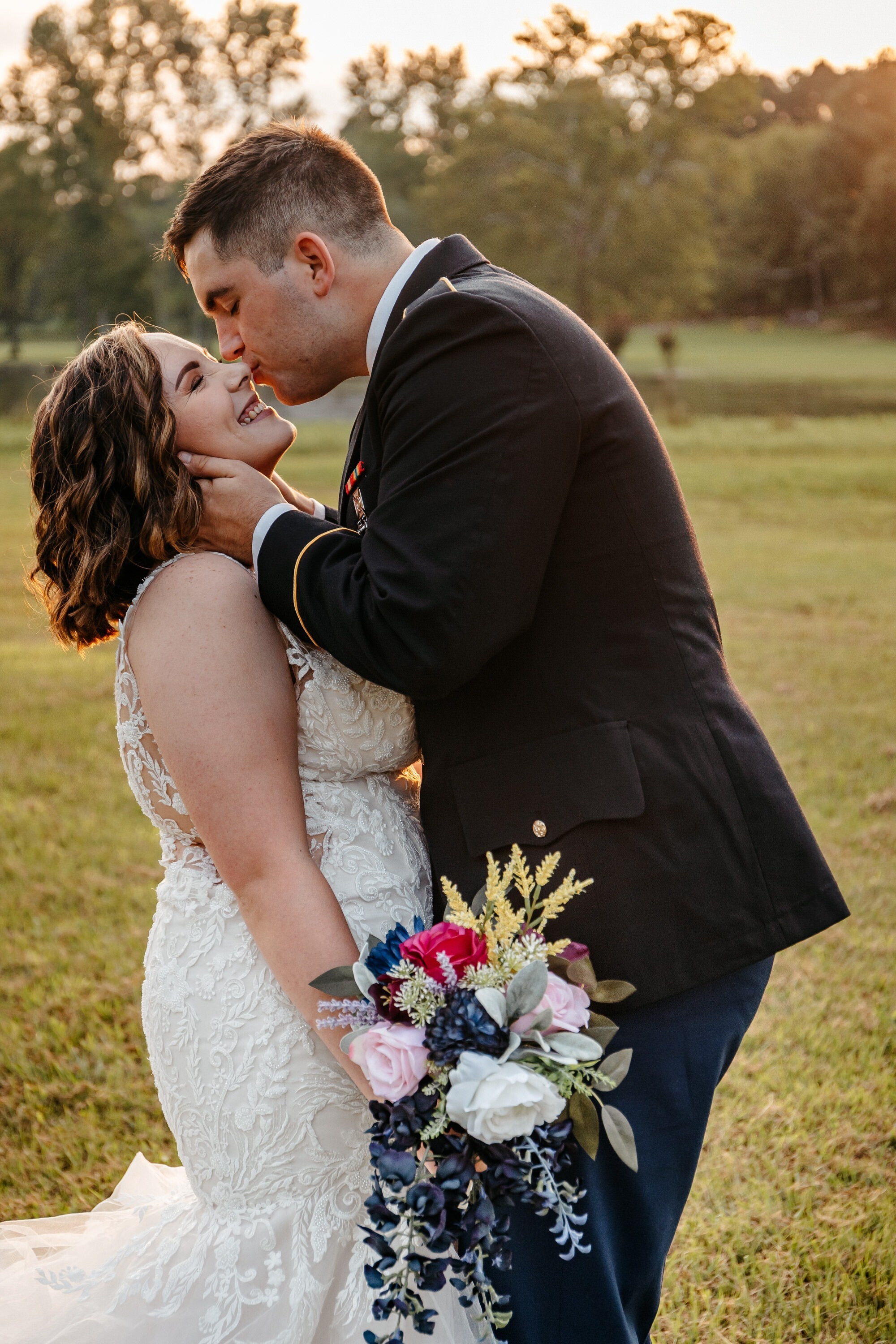 A groom wearing a military uniform kisses his bride while she holds a very colorful bouquet in one of many georgia outdoor wedding venues