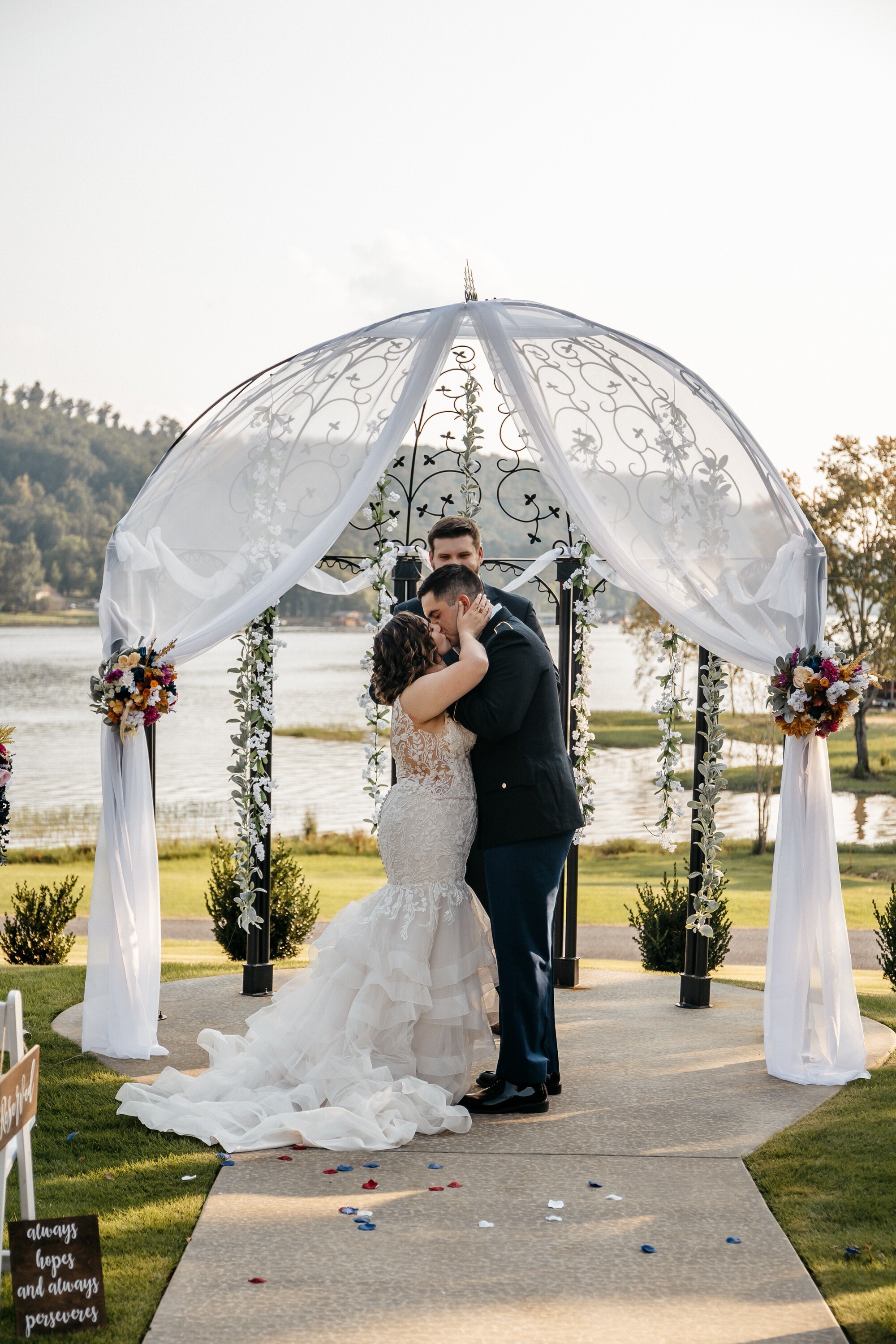 A bride and groom kiss after saying I do at an altar decorated with red and white flowers and white tule at one of the best outdoor wedding venues in north georgia