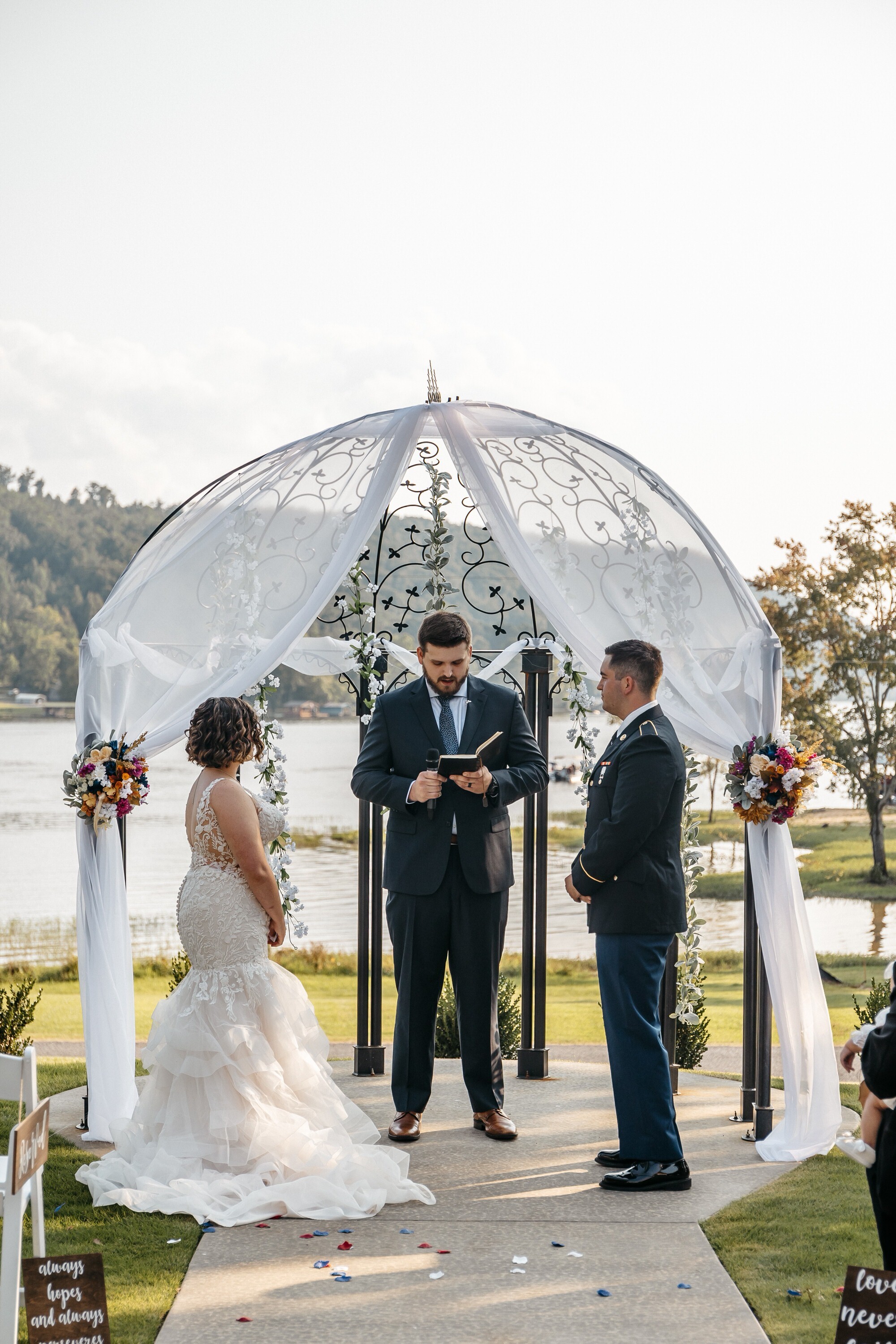 A bride and groom stands at an altar decorated with red and white flowers and white tule at one of the many outdoor wedding venues in georgia
