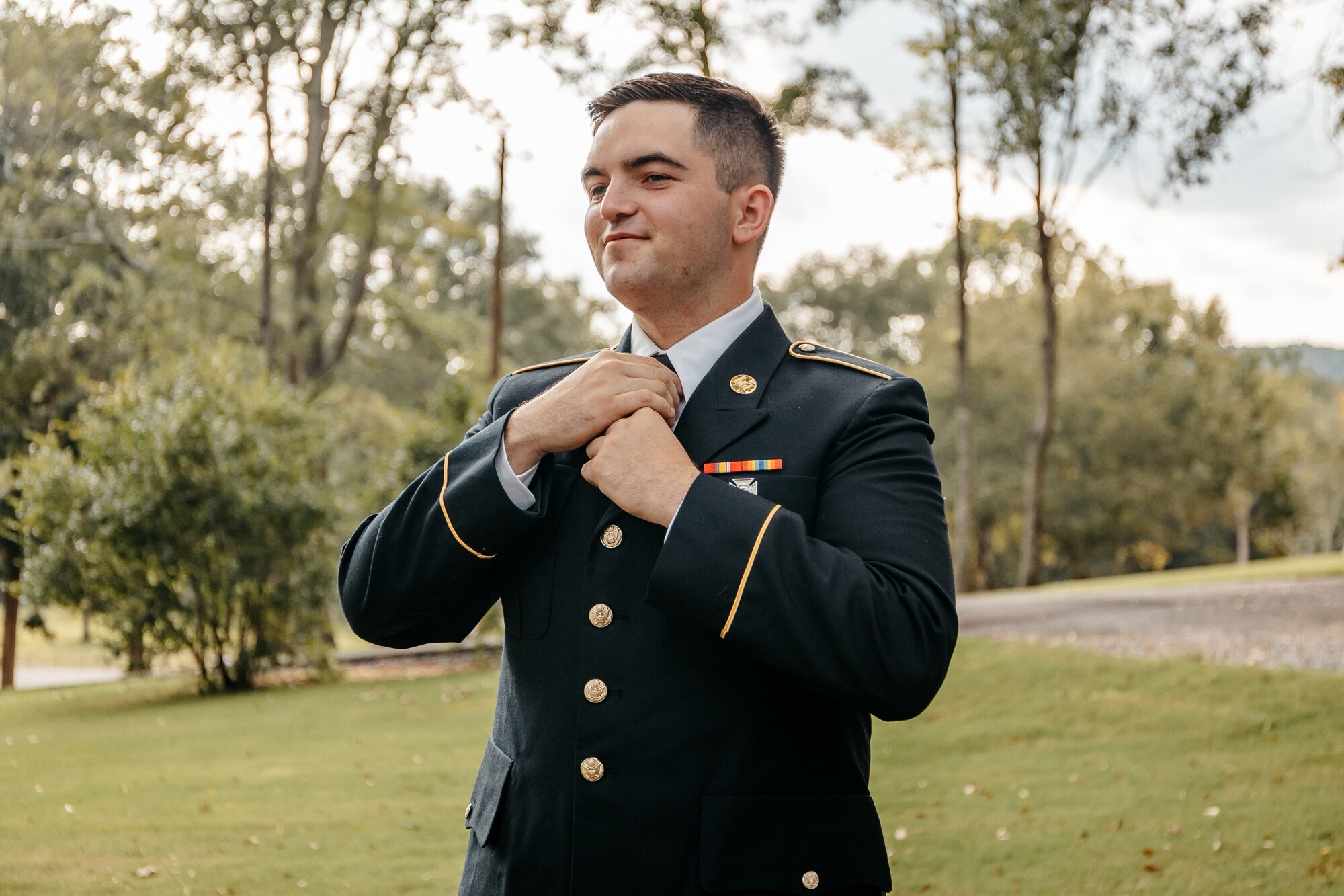 A man in a military uniform straightens his tie as he prepares for his ceremony at one of the best outdoor wedding venues in georgia