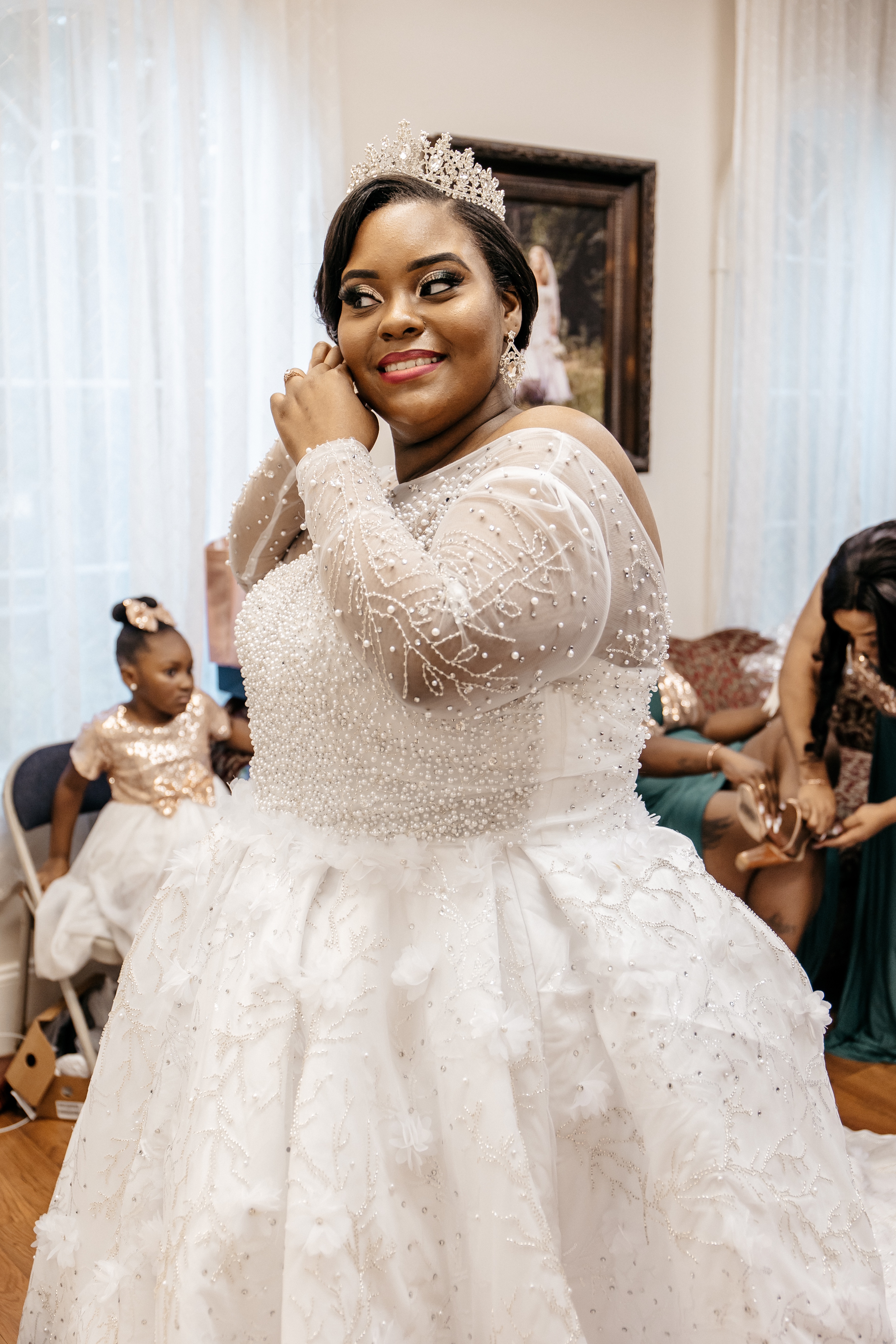 A bride wearing a tiara puts on her earrings while a micro wedding photographer takes photos