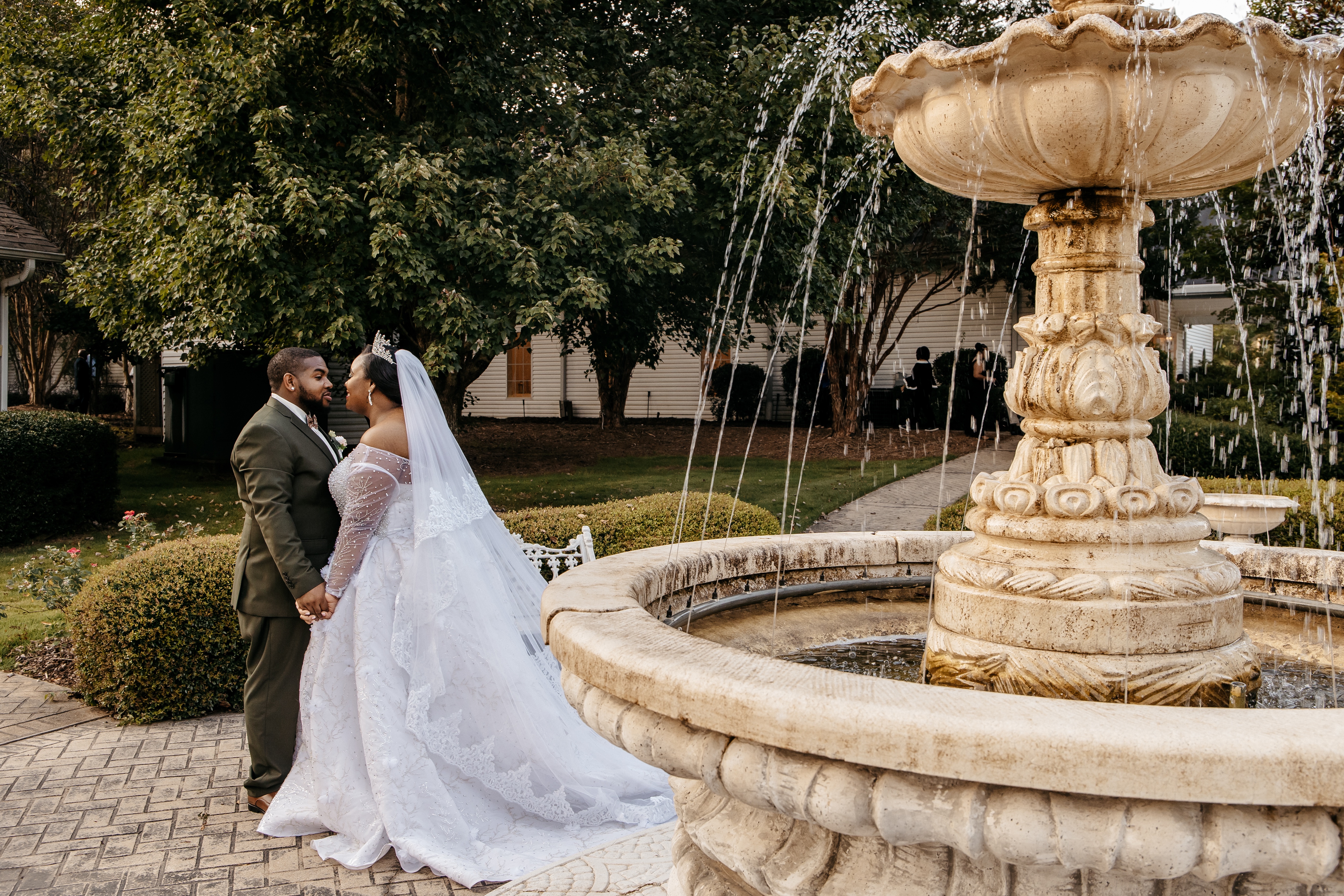 A bride and groom stand next to a large fountain in a beautiful garden at their micro wedding ceremony in north georgia